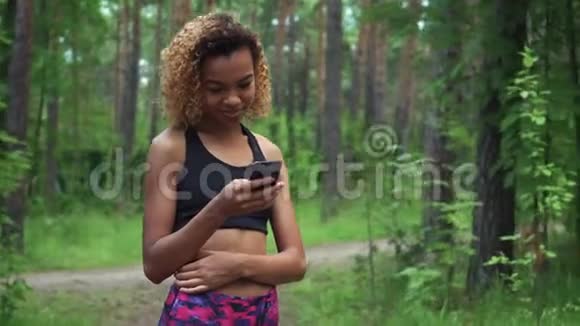 年轻漂亮的美国黑人卷发女士在慢跑前用手机聊天视频的预览图