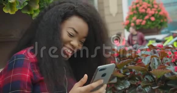 侧面情感肖像时尚快乐的年轻非洲女孩在享受音乐的同时通过手机发短信视频的预览图