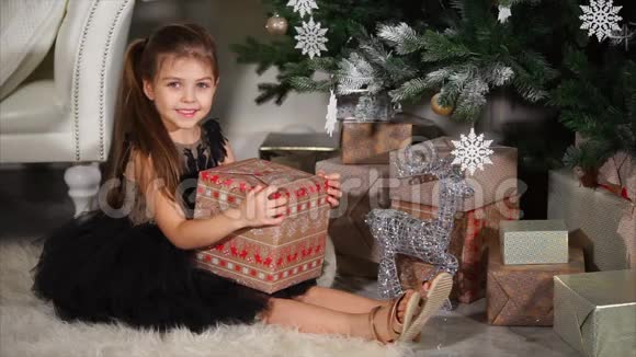 小大眼睛女孩正拿着一个大盒子里面放着圣诞礼物坐在云杉下视频的预览图