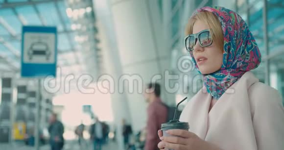 侧面肖像的迷人时尚金发女人戴着围巾的头和太阳镜她喝咖啡是通过视频的预览图