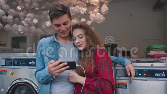 一对漂亮的夫妇在洗衣店里听电话里的音乐看有趣的视频故事英俊的年轻人视频的预览图