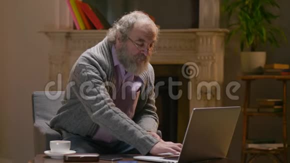 退休人员在笔记本电脑上一只手指打字坐在乡下温暖的小屋里视频的预览图