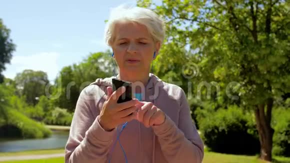 戴着耳机的老妇人在夏季公园跑步视频的预览图
