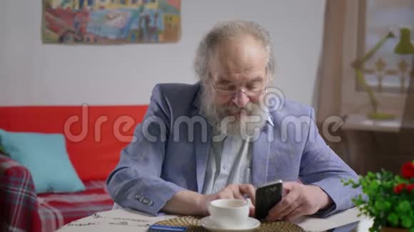 英俊的长胡子男人在他舒适的客厅喝茶读文章视频的预览图