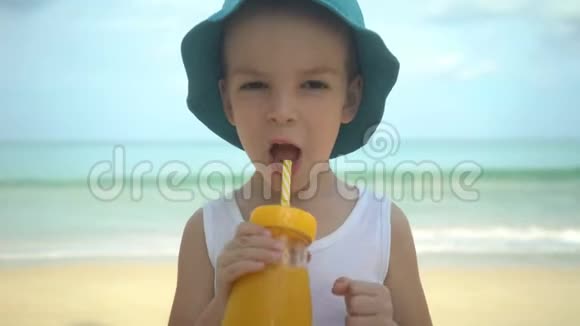 可爱的小男孩在海滩上喝着新鲜的热带芒果奶昔夏季概念视频的预览图