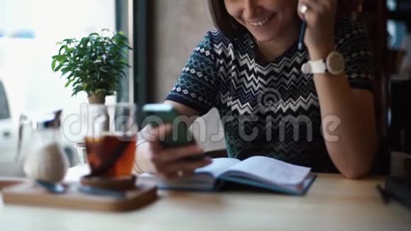 那个年轻的微笑女孩坐在咖啡馆里聊天发短信和浏览手机她很享受视频的预览图