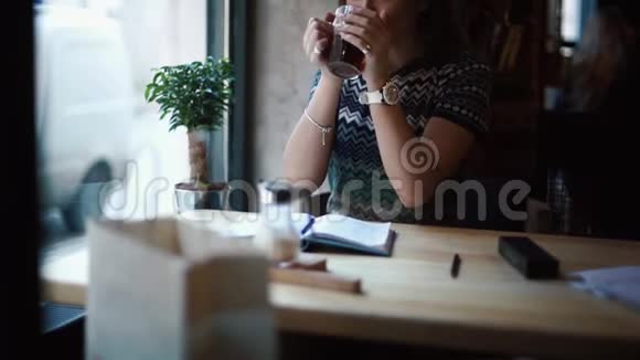 可爱快乐的年轻女子正享受着这杯茶透过窗户的咖啡馆看着视频的预览图