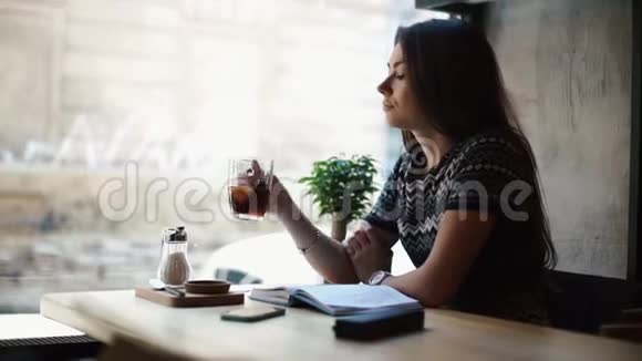 迷人的女孩正在享受这杯茶而透过咖啡馆的窗户她正在读她的笔记视频的预览图