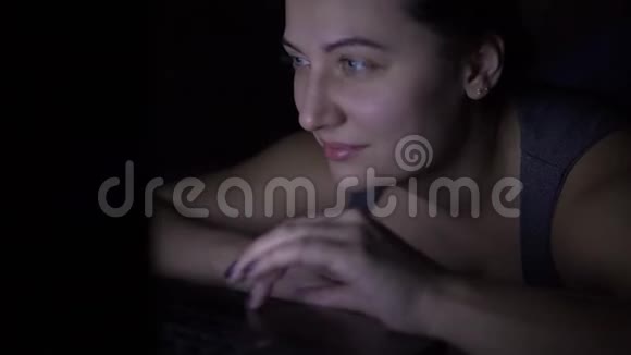 晚上躺在床上用笔记本电脑键盘打字的快乐女人视频的预览图