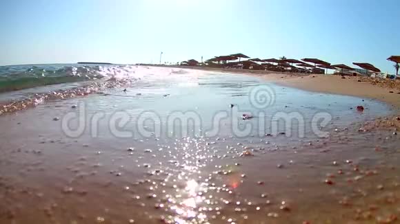 光波在沙滩上冲浪在晴朗的晴天带着茅草的海滩伞红海从下面看广角视频的预览图