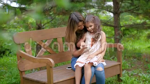 妈妈坐在长凳上她腿上有个小女孩女人带着孩子玩无忧无虑的笑开心的坐在上面视频的预览图