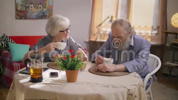 一对老年夫妇在他们舒适的餐厅里和一男一女愉快地聊天视频的预览图