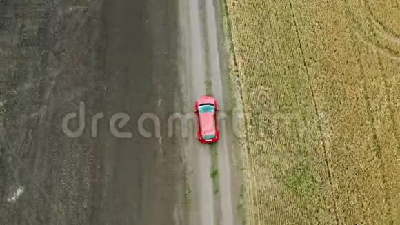 俯瞰着一片麦田和一辆红色的汽车在农村的道路上行驶视频的预览图