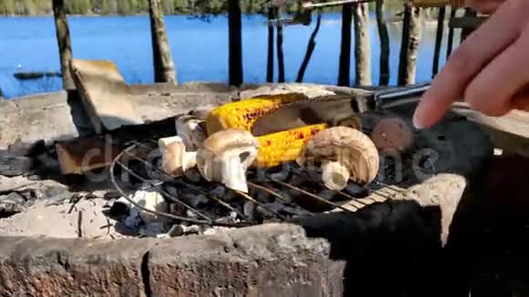 在一个美丽的阳光明媚的日子里在湖边的炭火混凝土烤箱上烤玉米和黑蘑菇视频的预览图