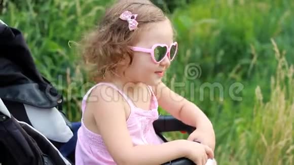 戴着太阳镜的快乐女婴坐在婴儿车里高兴极了视频的预览图