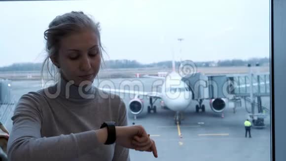 年轻旅游妇女在日程安排委员会寻找她的航班状况并检查机场智能手表的时间视频的预览图