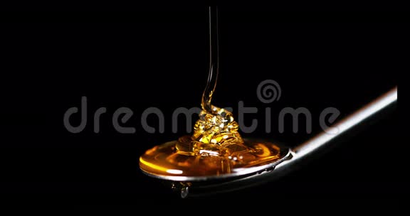 蜂蜜在黑色背景下的勺子上流动视频的预览图