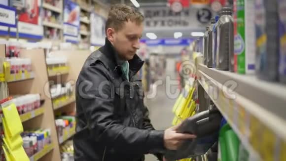 年轻人在维修服务站或超市为汽车选择机油货架上有不同的罐子视频的预览图