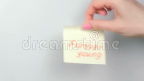 特写女人她的手贴着黄色的贴纸纸上面写着永远年轻的文字视频的预览图