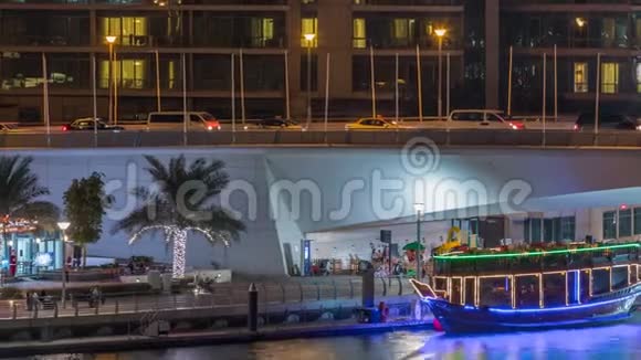 游艇和船只与游客停留在购物中心附近并通过桥下迪拜码头区的夜晚视频的预览图