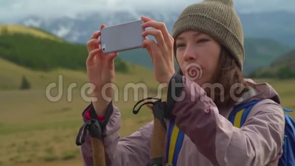 一个美丽可爱的阿桑旅游女孩用手机与美丽的多云高山拍照视频的预览图