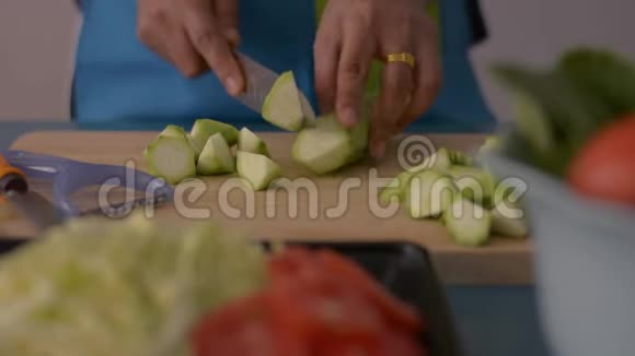 特写镜头中妇女的手在桌上的健康食品木制砧板上切有角的丝瓜视频的预览图