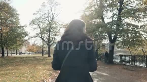 在秋天公园散步的年轻美丽的女人女孩在秋天沿着长廊行走生活方式的概念视频的预览图