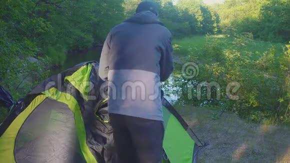 4k这个人在夏天的森林里把一个旅游帐篷放在河岸上视频的预览图