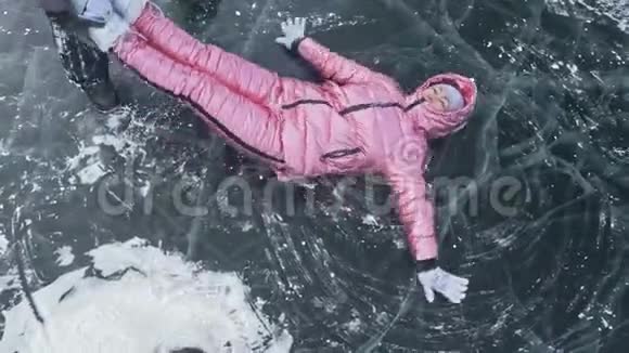 女孩飞起来在冰上翻滚在冰封的湖面上年轻夫妇在冬天散步时玩得很开心视频的预览图