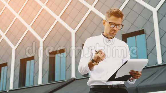 一个年轻的商人站在办公室手里拿着一个文件夹视频的预览图