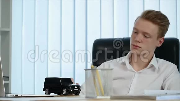 年轻的商人在办公室的桌子上玩一辆小汽车慢动作视频的预览图