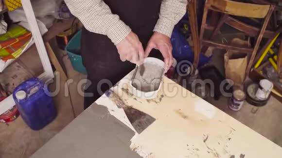老人的手在一个小塑料盒子里搅拌水泥视频的预览图