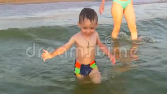 一个小男孩沿着海滩跑进她母亲的手臂镜头跟着他慢动作视频的预览图