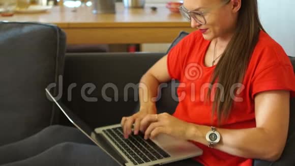 一个穿着红色连衣裙的女孩与社交网络通信舒适地坐在柔软的椅子上女性自由职业者视频的预览图