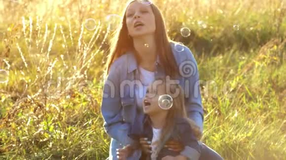 快乐的年轻母亲和女儿在公园里吹肥皂泡视频的预览图