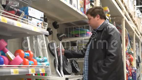 穿黑色皮夹克的胖子检查了超市货架上的杠铃的重量视频的预览图
