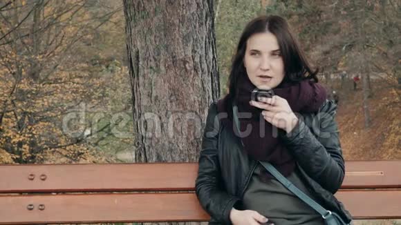 年轻的微笑妇女使用智能手机坐在公园的长凳上美丽的欧洲女孩打电话留言视频的预览图
