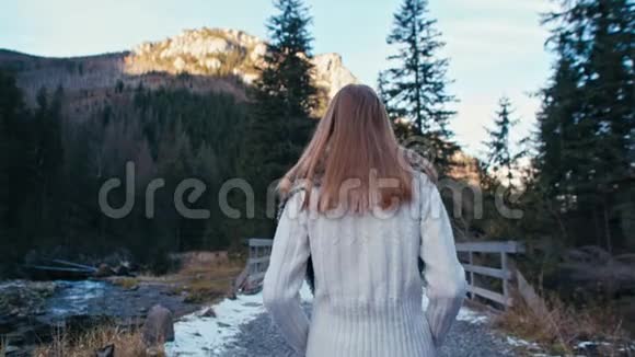 一位女士在山林中带着雪走在道路和桥梁上的后景视频的预览图