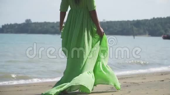 一个穿着美丽轻盈郁郁葱葱的绿色连衣裙的女孩正沿着海滩散步视频的预览图