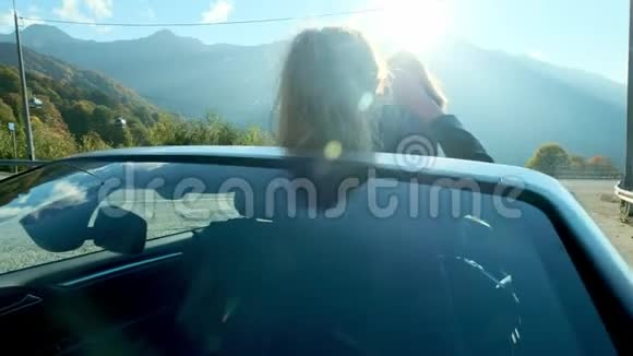 两个年轻漂亮的女孩戴着黑色眼镜穿着皮夹克坐在高山附近的红色敞篷车里他们制造了视频的预览图