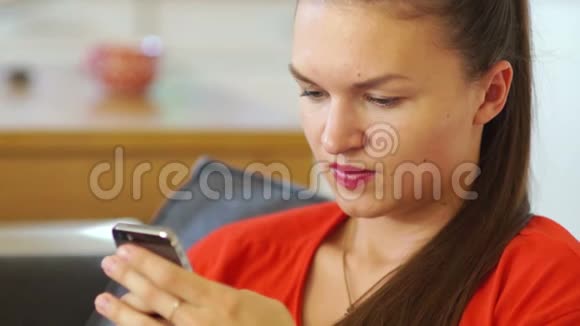 一个穿着红色裙子的年轻女孩对着手机屏幕微笑抬起头微笑社会网络视频的预览图