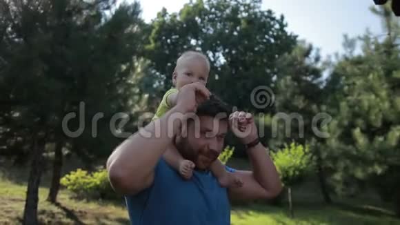 爸爸把可爱的小男孩扛在公园的肩上视频的预览图