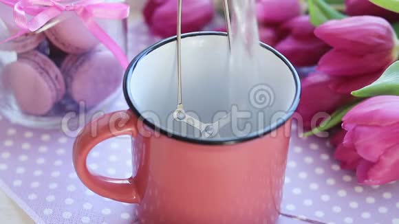 在粉红色陶瓷杯粉红色郁金香和红杏仁的茶袋上倒入热开水视频的预览图