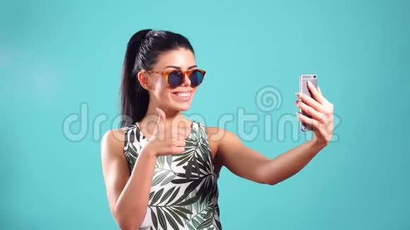 自信的年轻开朗的女孩一头直黑色的头发摆在蓝色背景上手里拿着智能手机视频的预览图