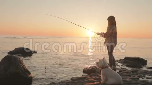 一个小女孩正在海上用鱼竿钓鱼一只小狗坐在它旁边海上日落视频的预览图