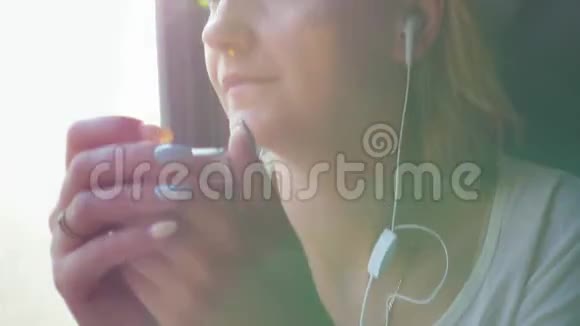 年轻的高加索女人坐在火车车厢里手里拿着智能手机听耳机音乐视频的预览图