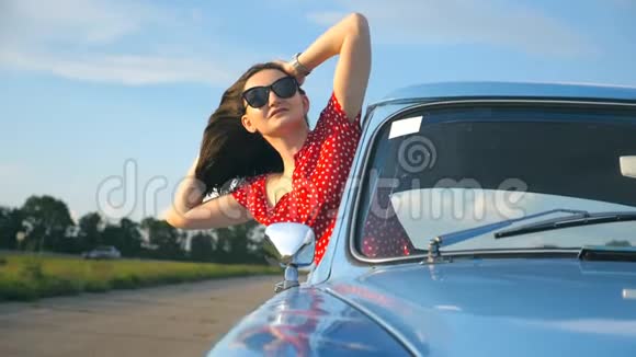 年轻女孩戴着太阳镜斜靠在老式车窗外享受旅行女人从复古汽车中脱颖而出视频的预览图