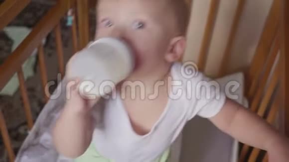 两岁的男孩在床上喝着塑料瓶里的牛奶视频的预览图