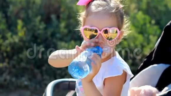 小女孩坐在婴儿车里从瓶子里喝水夏天口渴婴儿肖像特写视频的预览图