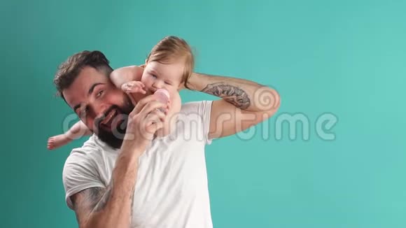 嬉戏的父亲带着他微笑的婴儿在蓝色背景的脖子上视频的预览图